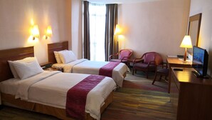A hotel room with two beds, a desk with a chair, a television, and two lamps.