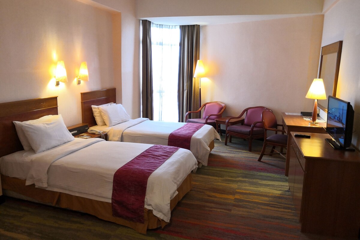 Habitación de hotel con dos camas, un escritorio con silla, televisión y dos lámparas.