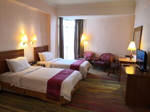 A hotel room with two beds, a desk with a chair, a television, and two lamps.