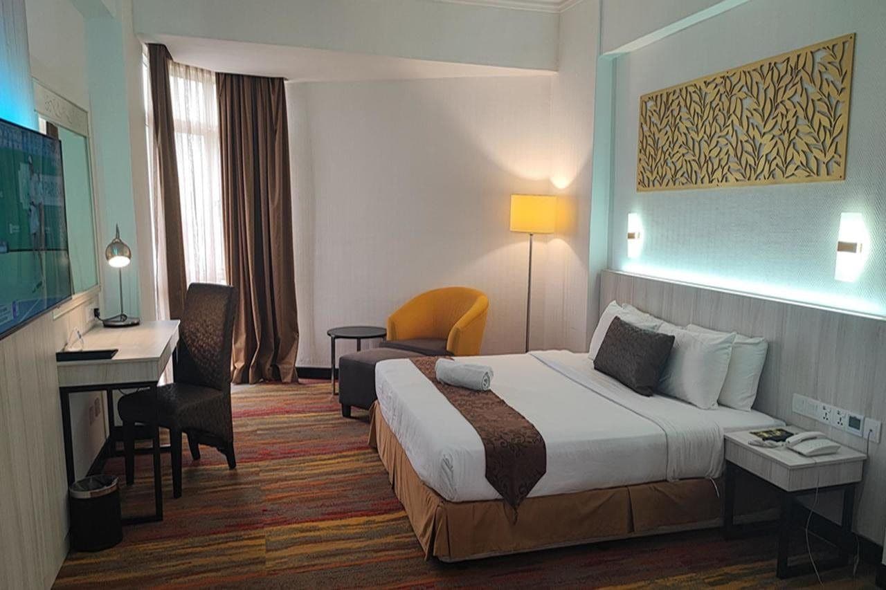Une chambre d’hôtel comprenant un lit, un bureau, une chaise, une lampe et un panneau décoratif mural.