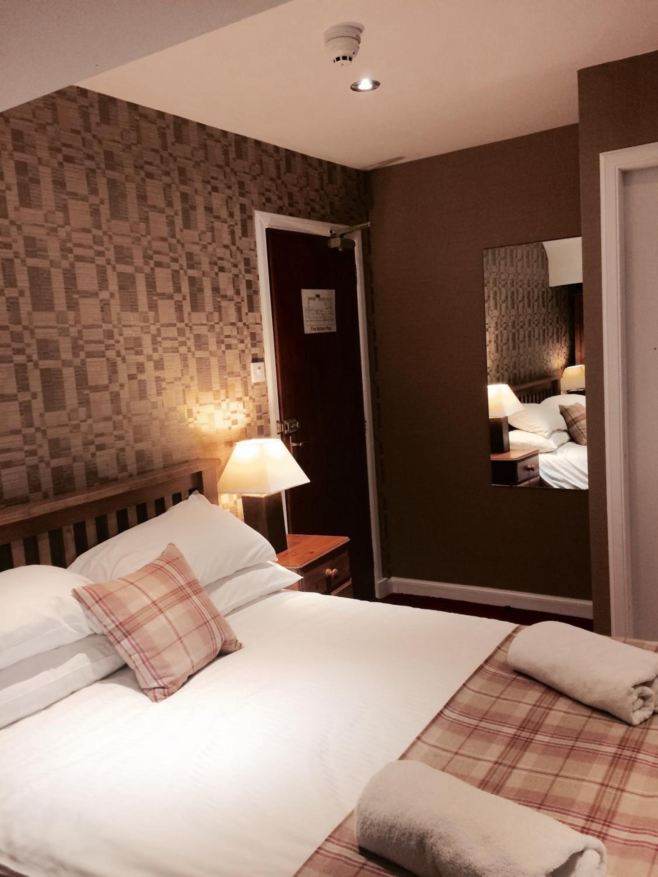 Una habitación de hotel con una cama, una mesita de noche, una lámpara, un espejo y una puerta.