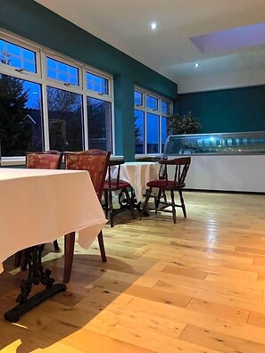 A dining area with wooden flooring, tables with white tablecloths, and chairs with red cushions.