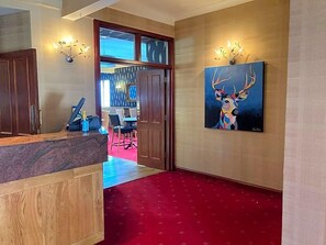A hotel lobby with a reception desk, a red carpeted floor, a painting of a deer, and a chandelier. - Panmure Arms (Brechin)