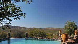 A clear blue pool with stone structures and terracotta pots. - Eagle Tented Lodge (Okaukuejo)