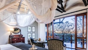 A bedroom with a bed, bedside table, chair, and a view of the outdoors through large windows. - Eagle Tented Lodge (Okaukuejo)