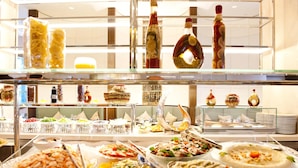 Un buffet con diversi piatti, tra cui pesce, insalate e dolci, disposti su numerosi vassoi.
