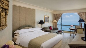 Una habitación de hotel con una cama grande, un sofá, una mesita y vista al mar.