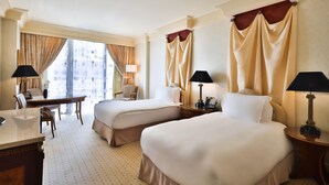 Habitación de hotel con dos camas, un escritorio, una silla y vistas a la ciudad.