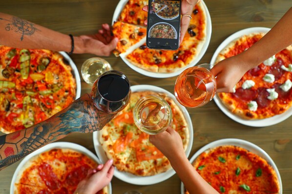 Un grupo de personas reunidas alrededor de una mesa con pizzas y vasos de bebidas.