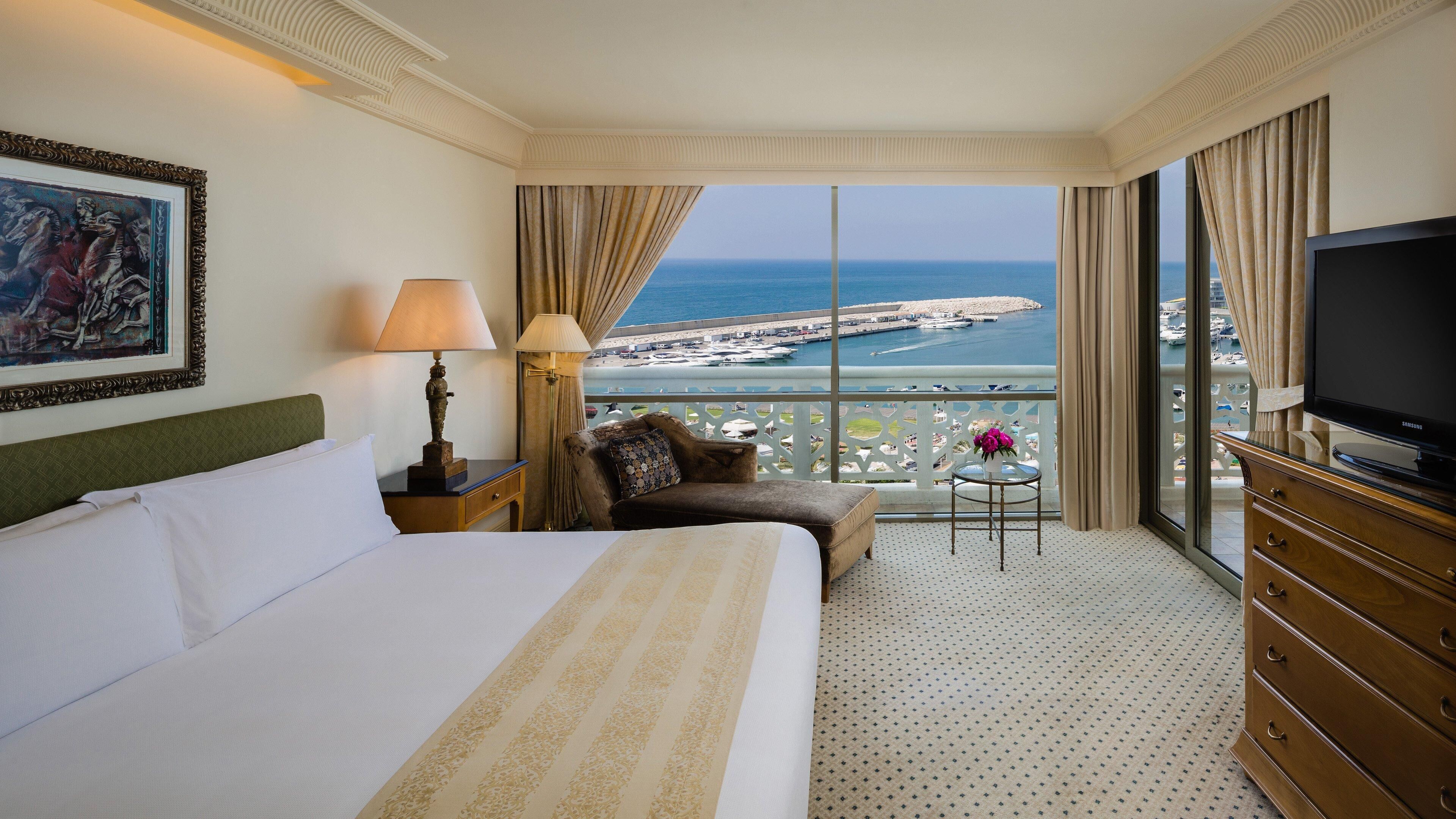 Camera d'albergo con un letto grande, un divano, una TV e un balcone con vista sul mare.