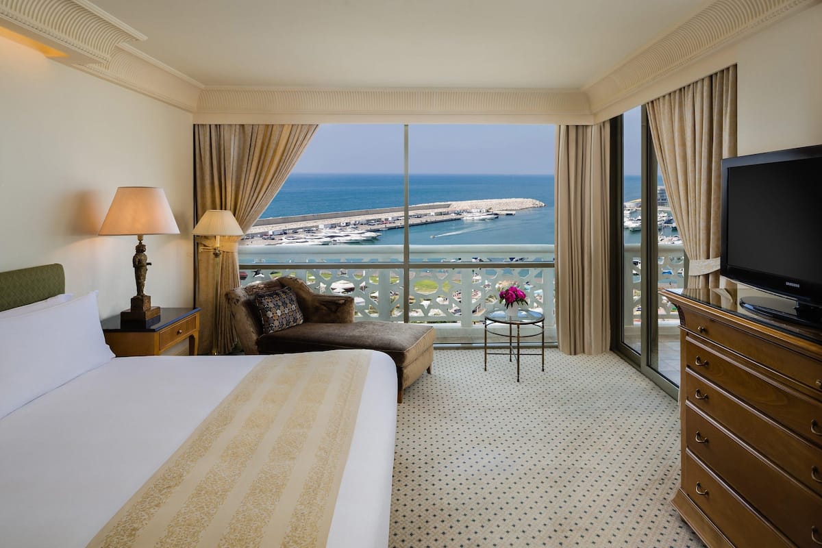 Habitació d'hotel amb un llit gran, un sofà, una televisió i un balcó amb vista al mar.
