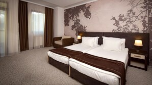 A hotel room with a large bed, two bedside tables with lamps, a chair, and a large window with curtains.