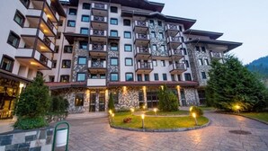 A multi-story hotel with balconies, a stone facade, and a landscaped entrance area.