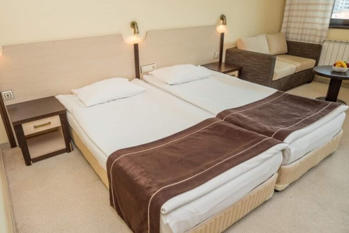A double bed with a brown blanket, a bedside table, a nightstand, a sofa, and a small table with fruit.