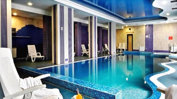 An indoor swimming pool with lounge chairs and a breakfast setup.