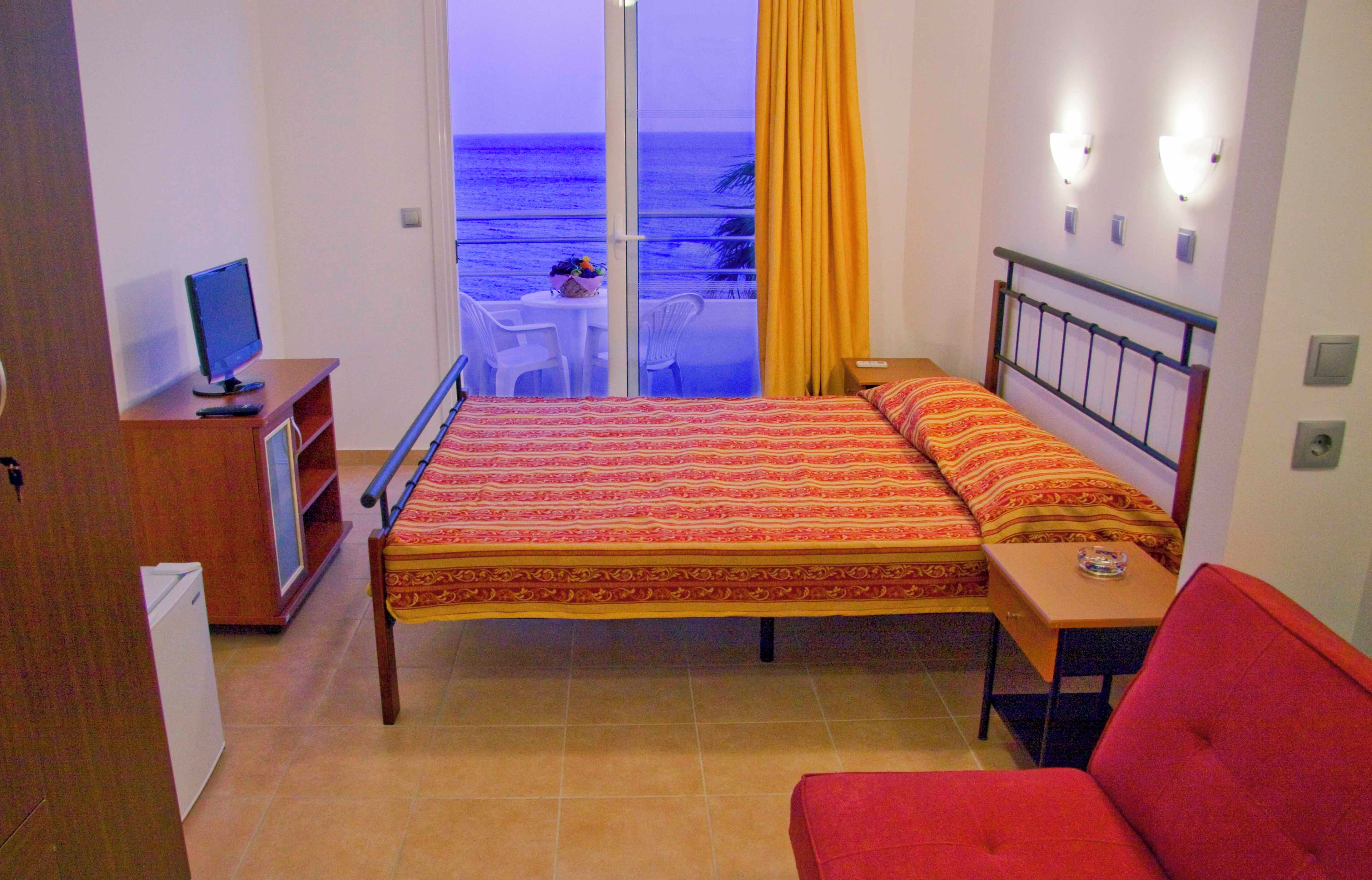 Una habitación de hotel con cama, escritorio, silla, televisor y vista a la playa.