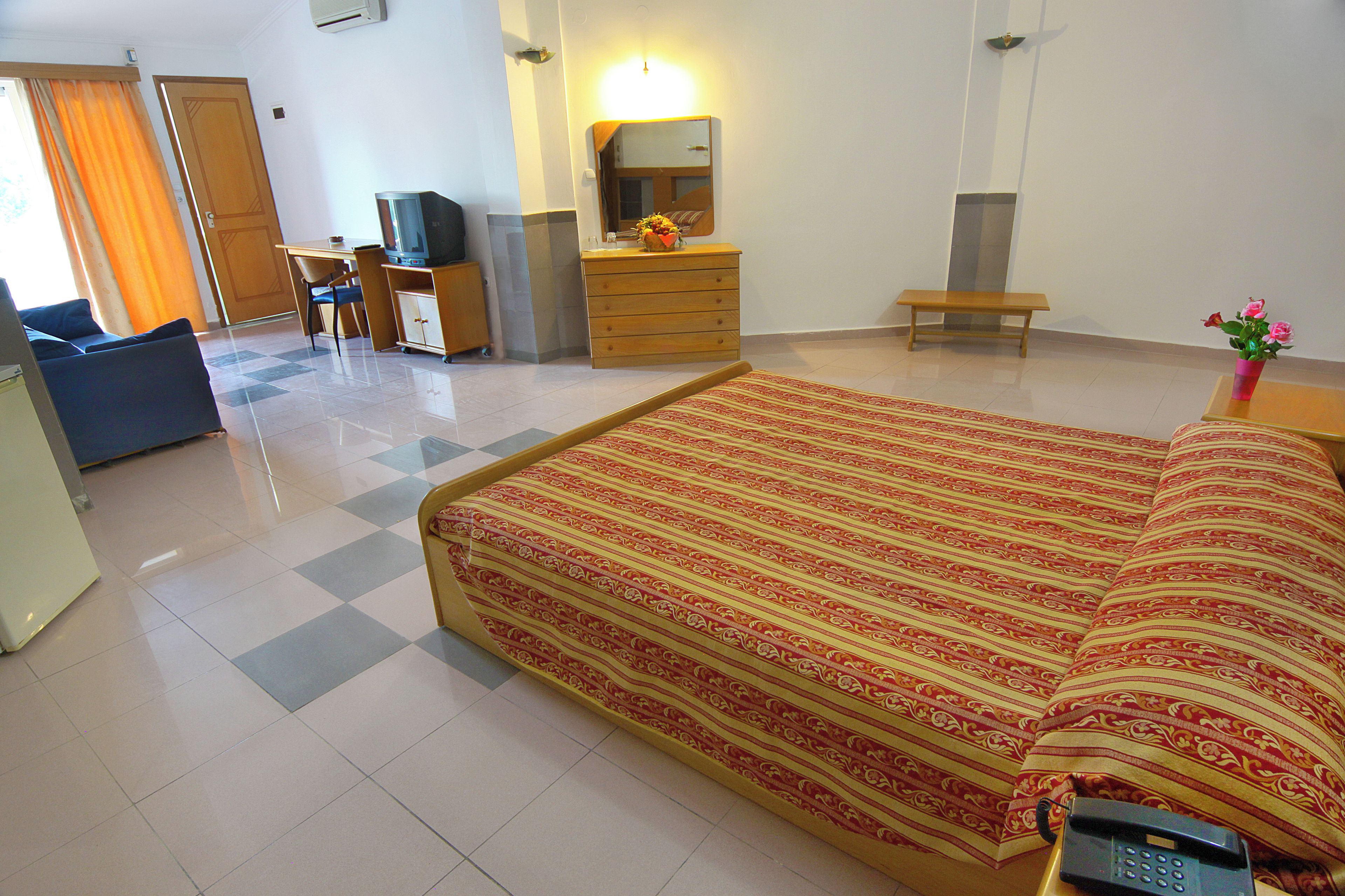 Ein Hotelzimmer mit einem Bett, einem Schreibtisch mit Computer, einem Sessel, einem Fernseher und einem Telefon.