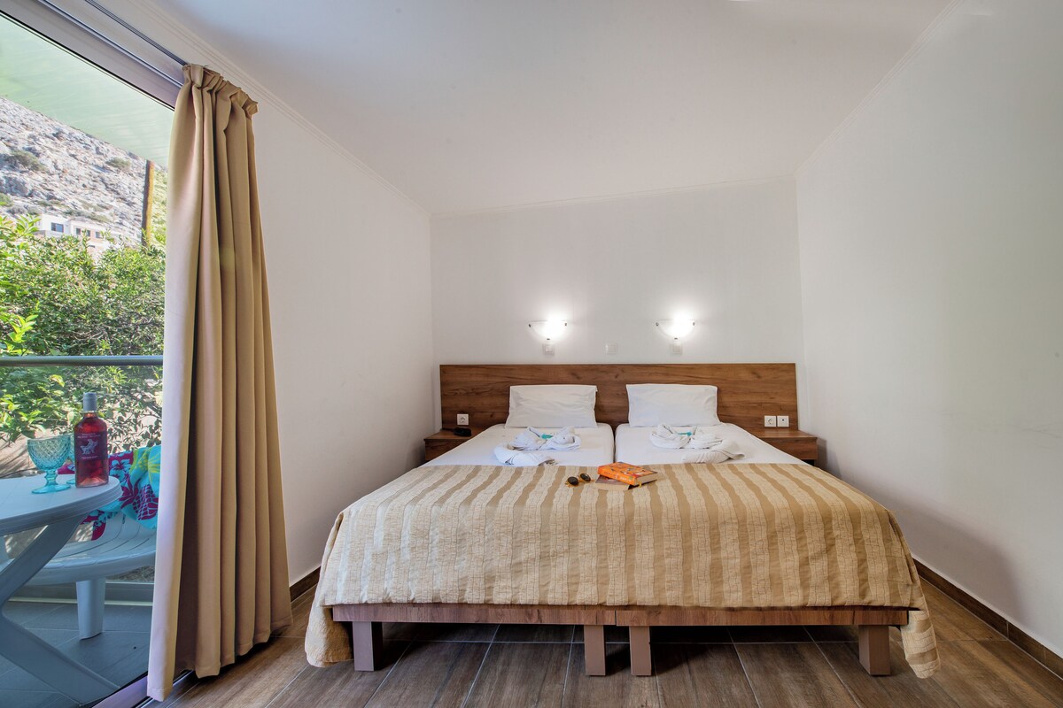 Habitación de hotel con una cama, dos mesitas de noche y vistas al exterior a zonas verdes.