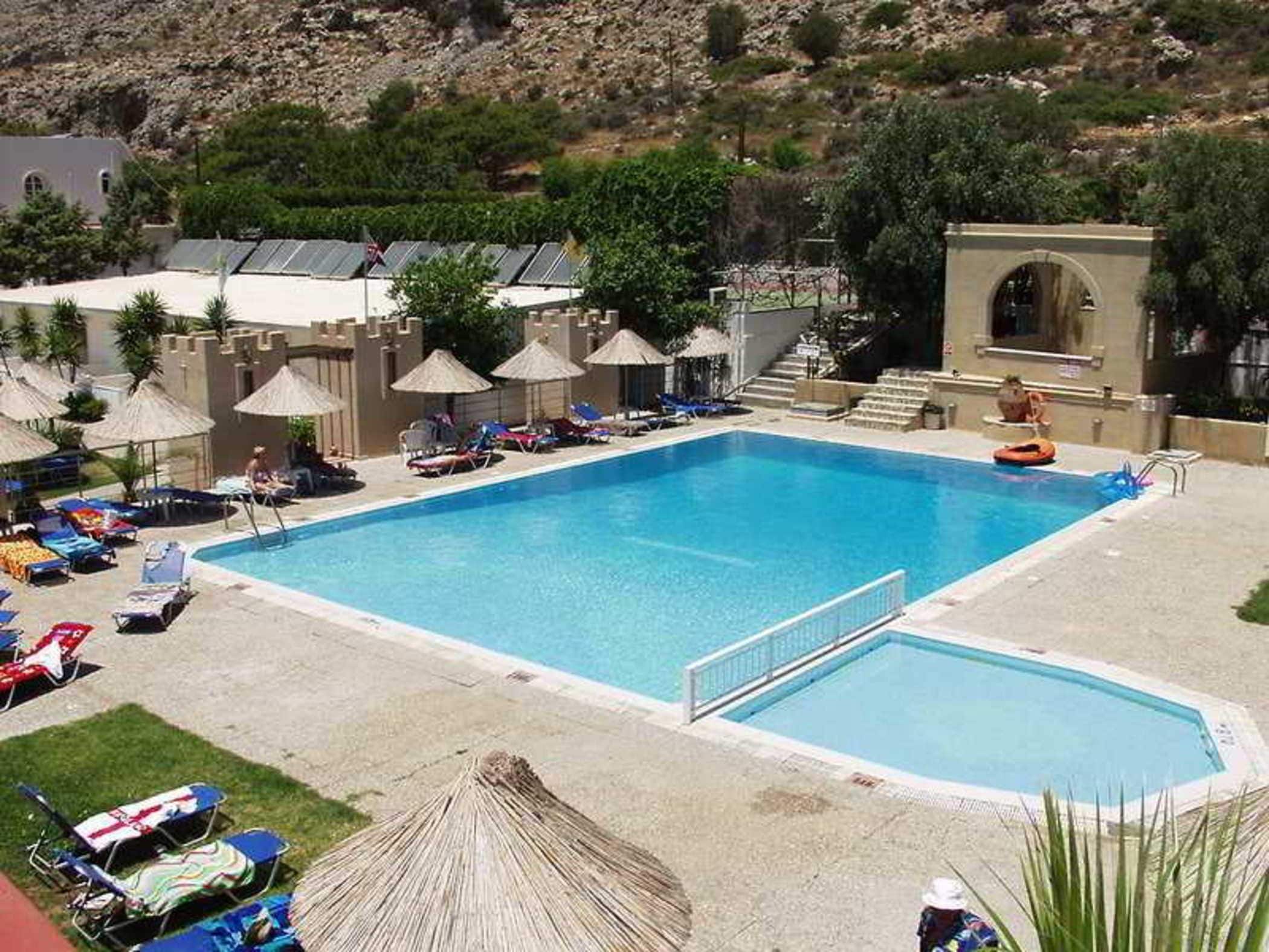 Piscina retangular com plataforma de mergulho, cercada por espreguiçadeiras e guarda-sóis.
