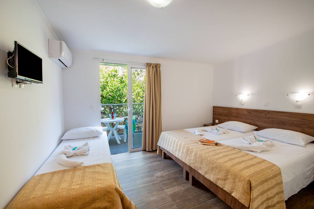 Habitación de hotel con dos camas, televisión y balcón con mesa y sillas.