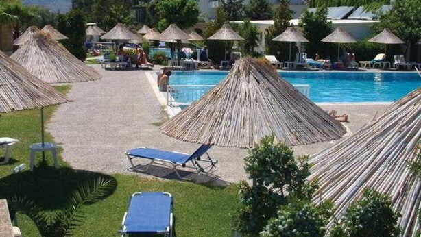 Ein Poolbereich mit Strohdächern, Liegestühlen und einem Gebäude im Hintergrund.