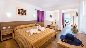 Ein Hotelzimmer mit einem großen Bett, einem Schreibtisch, einer Vase mit Blumen und Meerblick durch das Fenster.