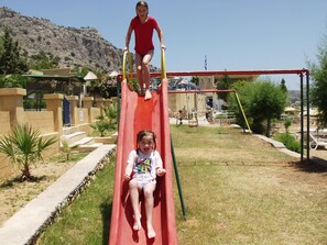 A playground with a red slide and a climbing structure. - Ilyssion (Rhodes)