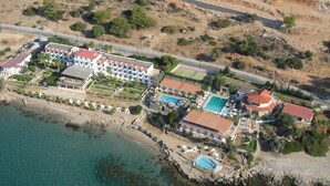 Luftaufnahme eines Küstenresorts mit mehreren Gebäuden, einem Strand und klarem, blauem Wasser.