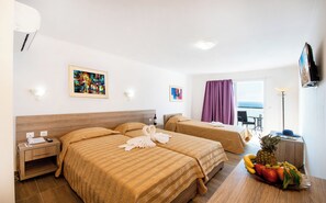 A hotel room with two beds, a small table with fruit, a desk with a lamp, and artwork on the walls. - Ilyssion (Rhodes)
