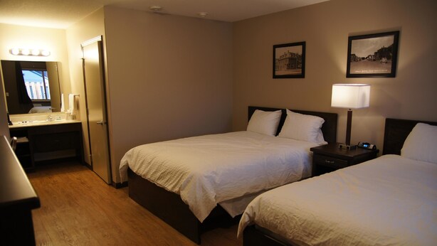 A hotel room with two beds, a bedside table with a lamp, a mirror, and a vanity with a sink. - Eden Valley Motel (Eden Valley)