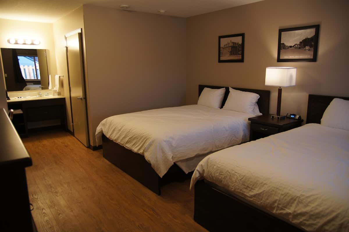 A hotel room with two beds, a bedside table with a lamp, a mirror, and a vanity with a sink.
