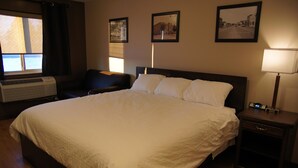 A hotel room with a large bed, a desk, a chair, a bedside table with a lamp, and a window with blinds. - Eden Valley Motel (Eden Valley)