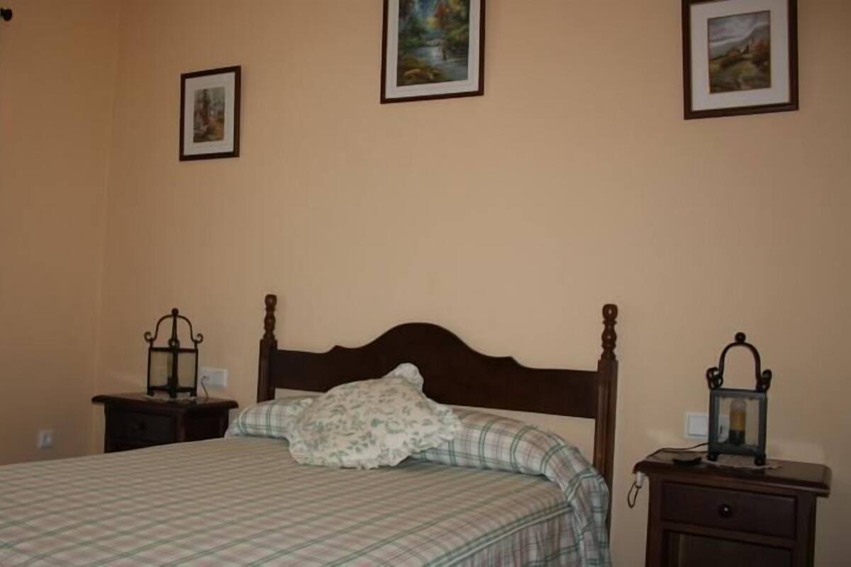 A bedroom with a bed, two nightstands, a window with curtains, and two framed pictures on the wall.