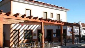 Ein Gebäude mit überdachter Terrasse, Sitzgelegenheiten im Freien und blauem Himmel.
