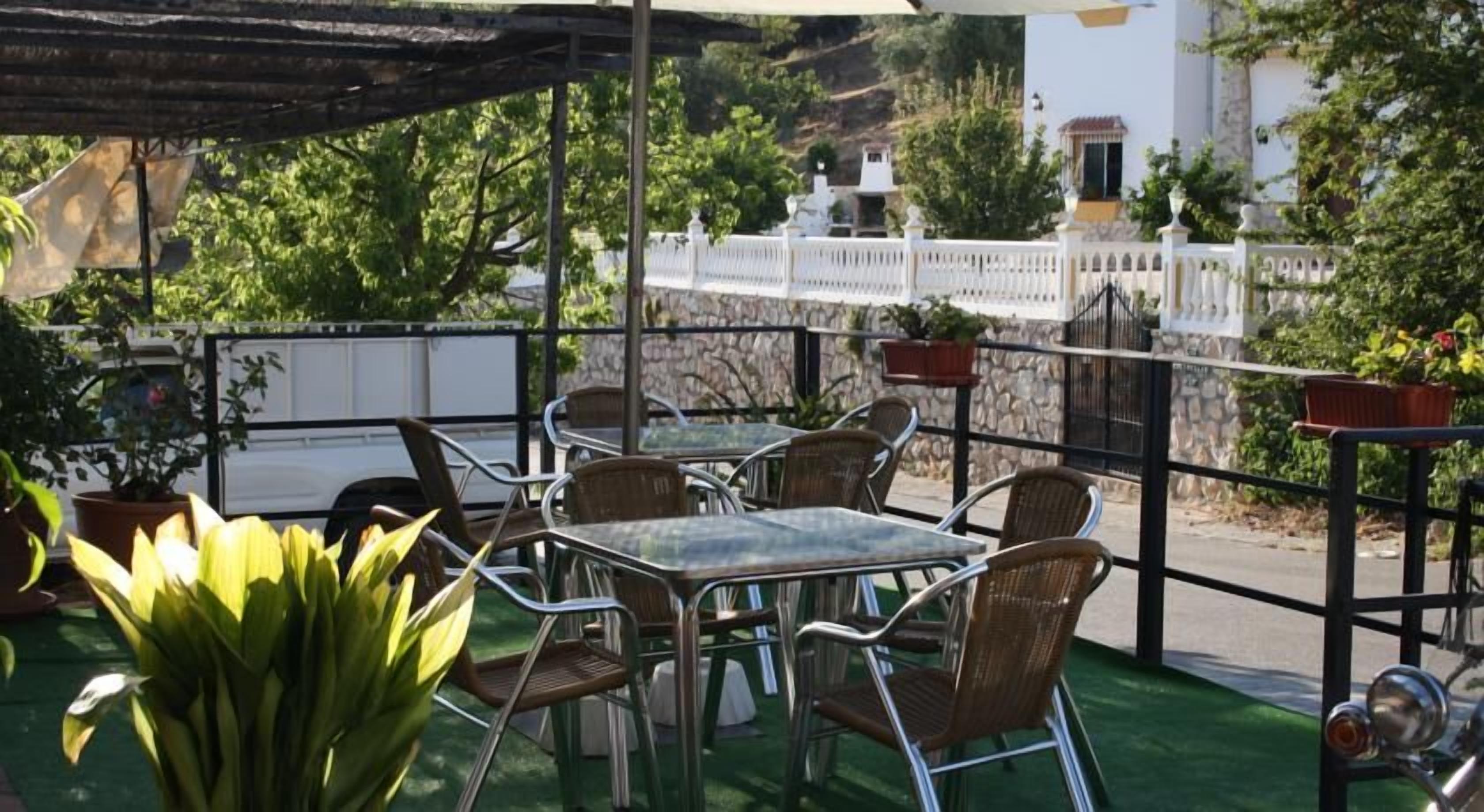 Un patio al aire libre con mesas y sillas, rodeado de plantas en macetas y una valla blanca.