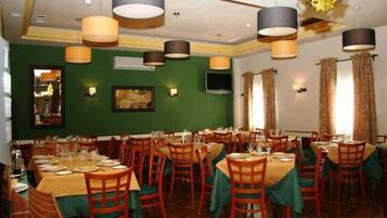 A restaurant with multiple dining tables and chairs, a green wall, and hanging pendant lights.