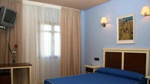 A hotel room with a bed, a desk, a television, and a painting on the wall. - Restaurante Atalaya (Minas de Riotinto)