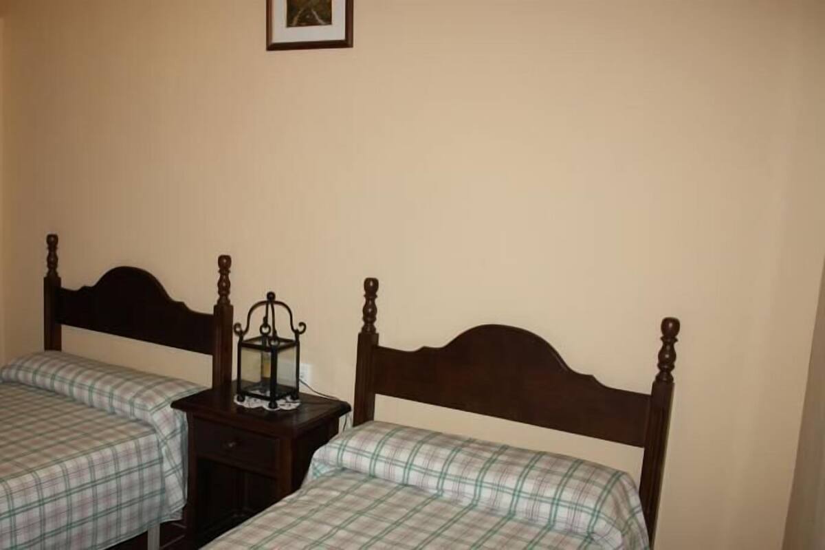Two single beds with wooden headboards, a small bedside table with a lantern, and a door.
