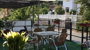 Une terrasse extérieure avec des tables et des chaises, entourée de plantes en pot et d’une clôture blanche.