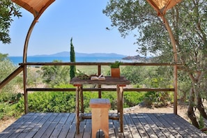 A wooden deck with a table and bench, overlooking a coastal landscape with trees and a distant view of the sea. - Gitavillage Talamone (Orbetello)