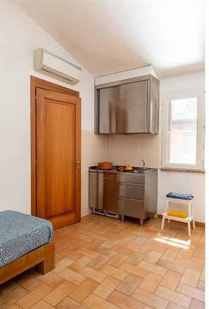 Una habitación pequeña con cama, kitchenette, puerta de madera y ventana.