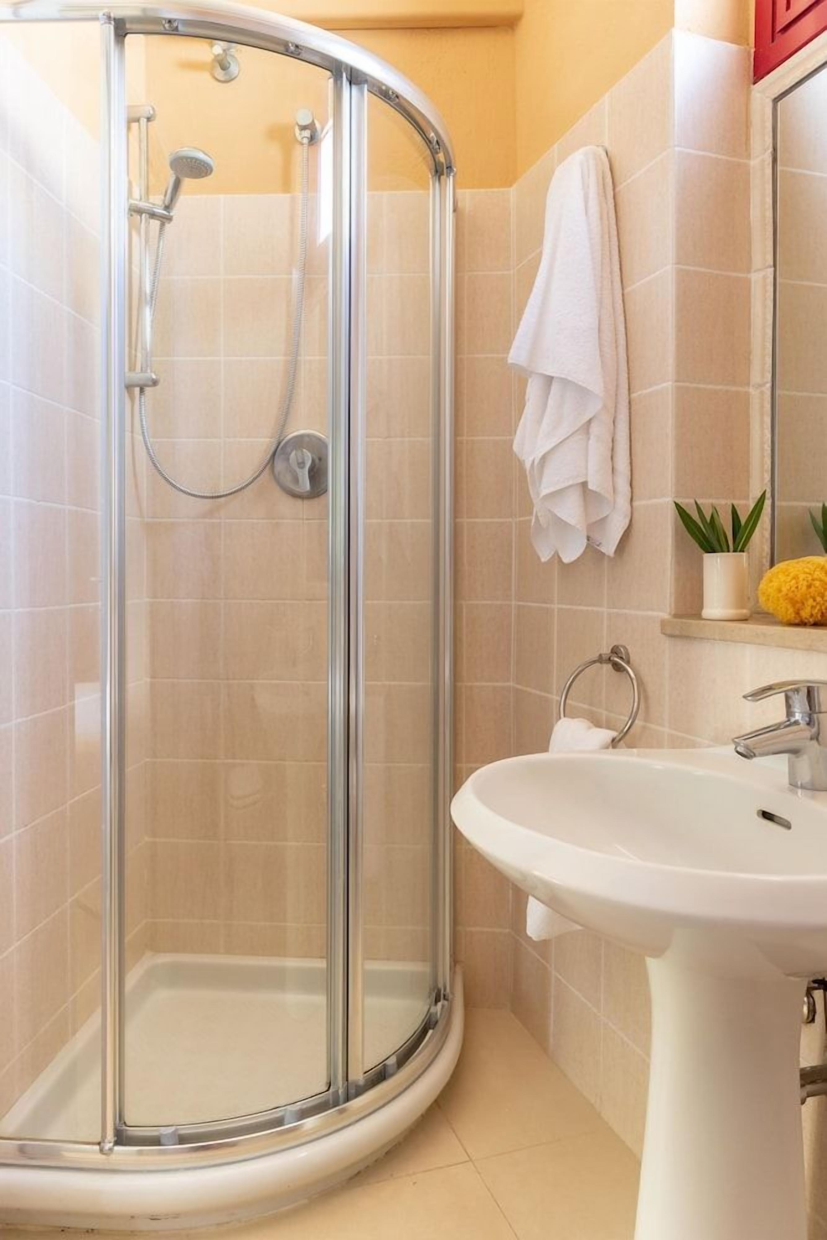 A shower with a glass door, a white sink, and a towel rack.