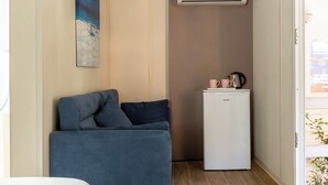 A compact room with a blue sofa, a small white refrigerator, and a ceiling-mounted air conditioner. - Gitavillage Talamone (Orbetello)