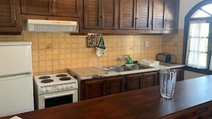 Una cocina con armarios de madera, una estufa blanca, un fregadero y una ventana con cortinas.