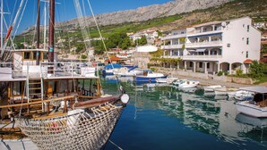 Un port de plaisance avec des bateaux amarrés, un grand voilier et des bâtiments dotés de balcons et de terrasses extérieures.