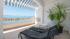Un balcon avec deux fauteuils de jardin, un pot de fleurs et une vue sur la mer.