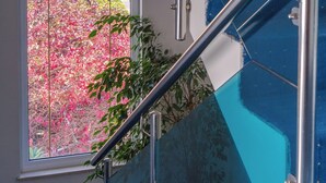 Un escalier avec des rampes en verre, offrant une vue sur des arbustes à fleurs roses à l’extérieur.