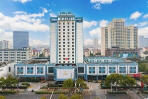 Un hotel de varios pisos con una torre central, rodeado de otros edificios, y un cielo despejado.