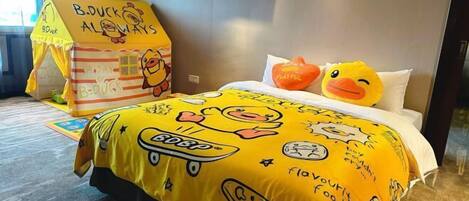 A hotel room with a bed covered in yellow bedding featuring duck-themed designs, a small playhouse, and a pillow with a duck design.