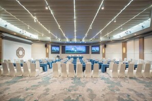 Een vergaderzaal met een lange tafel, rijen stoelen en meerdere schermen aan de wanden.